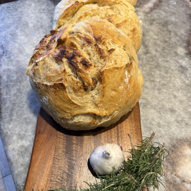 Rosemary and garlic sourdough loaf on a board with fresh rosemary and a head of garlic